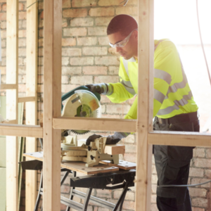Medewerker in bedrijfskleding die tijdens zijn klus op de projectplaats gebruik maakt van geleende afkortzaag.
