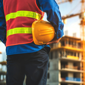 Bouwvakker kijkt naar gebouw in steigers met zijn veiligheidsvest aan en helm onder zijn arm